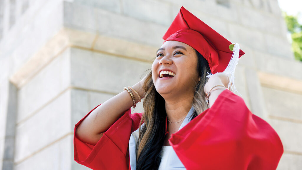 A student in red robes stands near the Memorial Belltower.