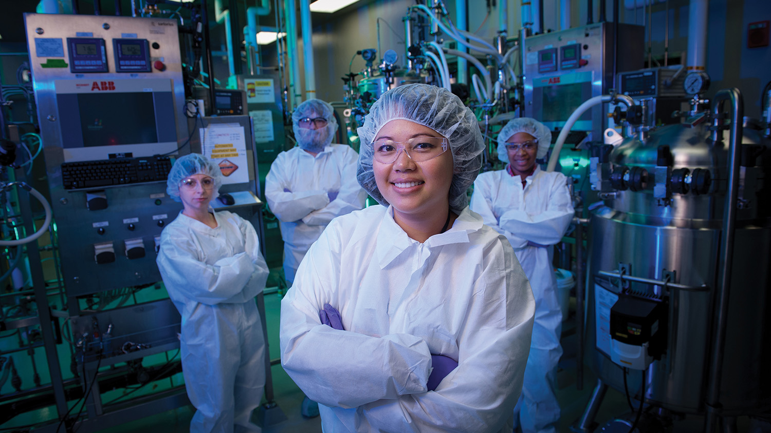 A group of researchers in white coats stand in a lab.