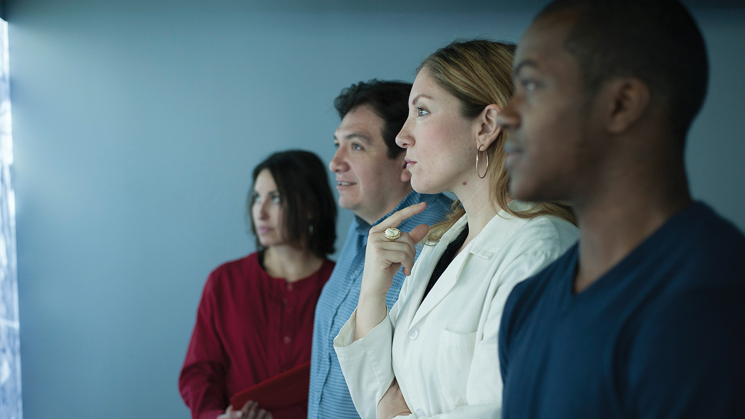 Faculty stand in profile looking at a screen.