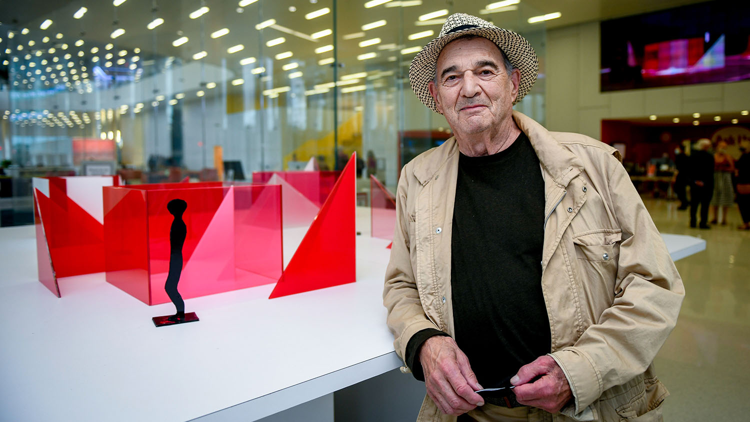 Photo features artist Larry Bell standing in front of a maquette of his "Reds and Whites" installation slated for Centennial Campus, featuring red and white sculptural blocks, in the lobby of Hunt Library.