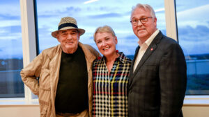 Photo features artist Larry Bell posing beside Randy and Susan Woodson in the lobby of Hunt Library.