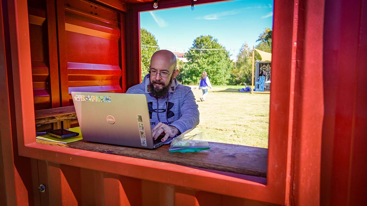 A man works on his laptop in the red shipping container at The Corner.