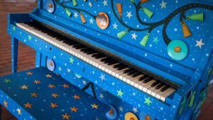 A piano painted cobalt blue and decorated with stars, located on The Corner's main stage.