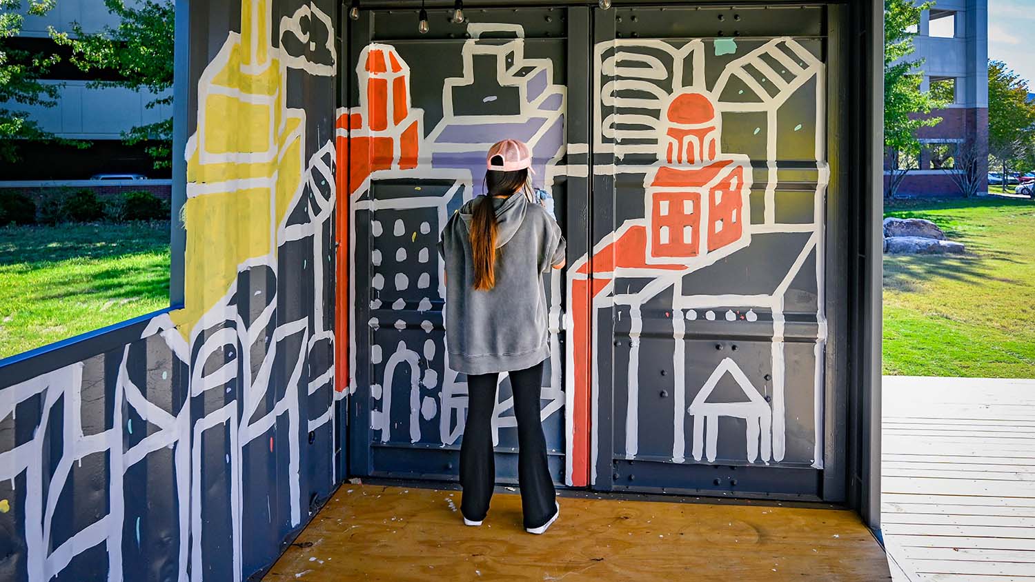 A student paints a mural in the interior of one of The Corner's shipping containers, adding a splash of color and visual interest.