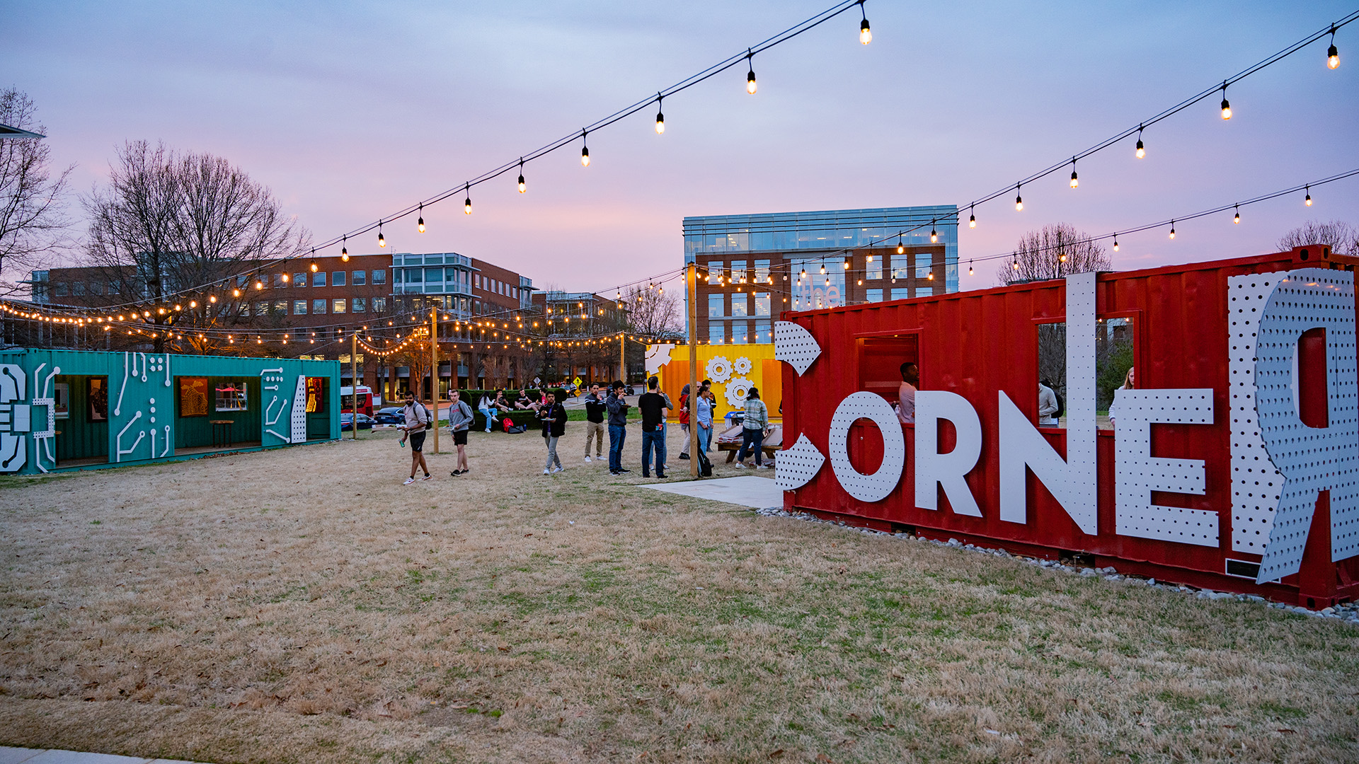 Students roam between shipping containers in The Corner at dusk.